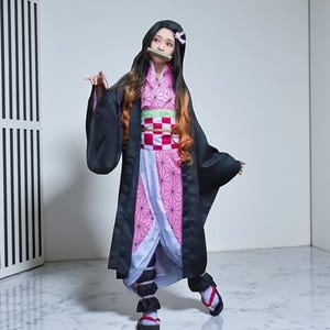May include: A cosplay costume featuring a black kimono with long sleeves, a pink and white patterned under-kimono, and a green and red obi. The character has long black hair with orange highlights and a bamboo muzzle.