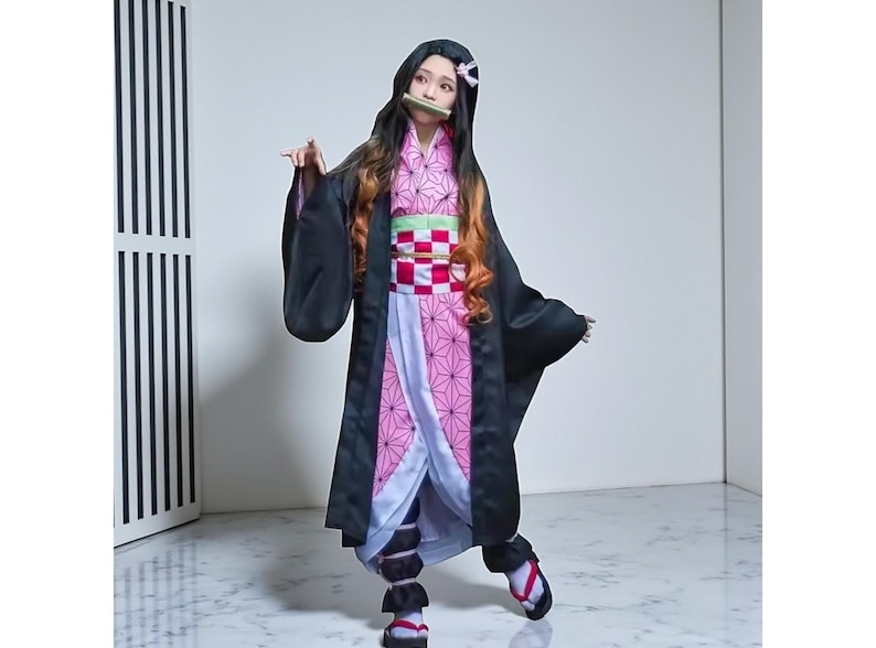 May include: A cosplay costume featuring a black kimono with long sleeves, a pink and white patterned under-kimono, and a green and red obi. The character has long black hair with orange highlights and a bamboo muzzle.