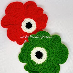 May include: Two crocheted flowers, one red and one green, with white and black centers.  The flowers are handmade and have a textured appearance.
