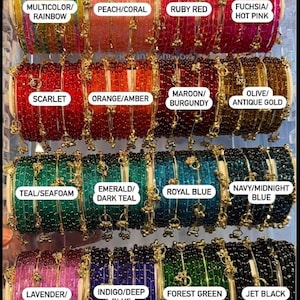 May include: A collection of colorful beaded bangles in various shades, including ruby red, emerald green, and navy blue. Each bangle is adorned with gold-colored accents. The image displays a variety of colors, with labels such as "Multicolor/Rainbow" and "Jet Black".