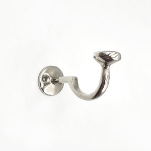 May include: A silver metal hook with a round base and a curved arm. The hook is designed for mounting on a wall.