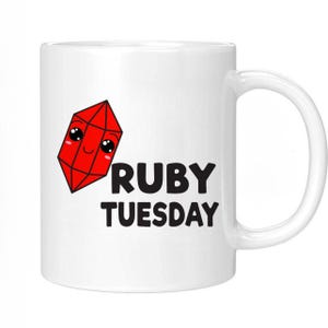 May include: White ceramic mug featuring a red cartoon ruby gemstone with a smiling face and the text "RUBY TUESDAY" in black.