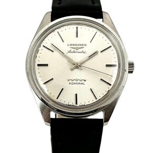 May include: A silver Longines Admiral automatic wristwatch with a white face and black hands. The watch has a black leather band.