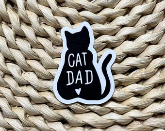 May include: Black and white sticker with a silhouette of a cat sitting with the text "CAT DAD" and a small heart.