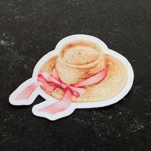 May include: A straw hat with a pink ribbon tied around it. The hat is light brown and has a woven texture.