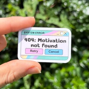 May include: A rectangular sticker featuring a computer pop-up window design with the text SYSTEM ERROR and 404: Motivation not found. The sticker includes a pink Retry button and a blue Cancel button, accented with pastel rainbow stripes.