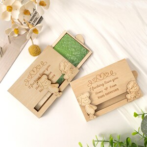 May include: Two wooden anniversary cards with the text "I fucking love you" and "Henry Evian Happy Anniversary" engraved. Each card features a sliding wooden figure and a green block inside.