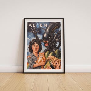 May include: A framed art print titled ALIEN featuring a person with curly dark hair wearing a grey uniform with a rainbow patch, holding an orange tabby cat. Behind them, a black creature with an open mouth and sharp teeth looms large.