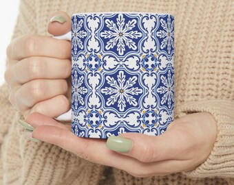 Op de afbeelding: Witte keramische mok met een geometrisch patroon in blauw en wit. Het patroon heeft een herhalend ontwerp van gestileerde bloemen en bladeren.