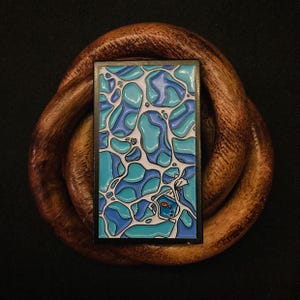 May include: A blue and white enamel pin with a fish in a bowl design. The pin is surrounded by a black border.