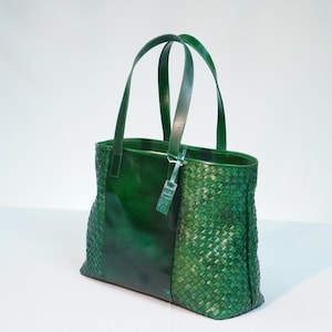 May include: A green leather tote bag with a woven design. The bag has two top handles and a zipper closure.