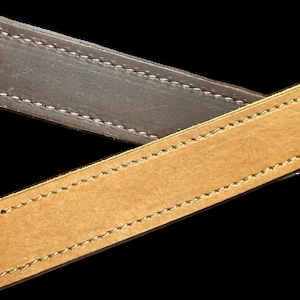 May include: Two leather straps, one brown and one tan, with stitching around the edges. The straps are crossed over each other.
