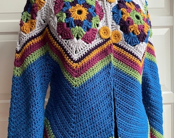 May include: A blue crocheted cardigan with a colourful geometric pattern on the front and a zip closure. The cardigan has a collar and long sleeves.