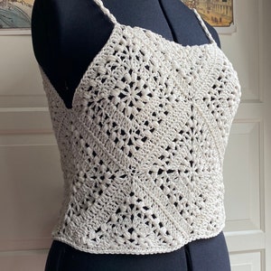 May include: A white crocheted tank top with a geometric pattern. The top is sleeveless and has a scoop neck.