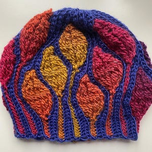 May include: A crocheted hat with a colorful abstract design featuring shades of blue, red, orange, and yellow.
