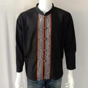 Könnte beinhalten: Ein schwarzes Langarmhemd mit einem geometrischen Muster in Weiß, Orange und Rot auf der Vorderseite. Das Hemd hat einen Stehkragen und einen Knopfverschluss.