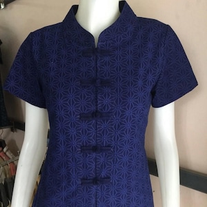 May include: A navy blue short-sleeved shirt with a geometric pattern and a mandarin collar. The shirt has five black buttons with a knot detail.