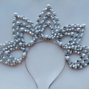 May include: A silver headband with a flower design made of white pearls and rhinestones.