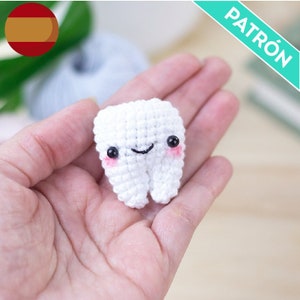 May include: A white crocheted tooth with a smiling face and pink cheeks. The tooth is being held in a hand.
