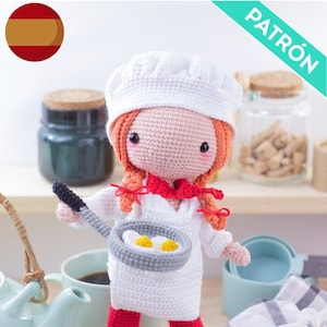 May include: A crocheted doll dressed as a chef, wearing a white hat and uniform, holding a frying pan with two fried eggs. The doll has red hair and a red scarf. The word "PATRÓN" is visible in the upper right corner.