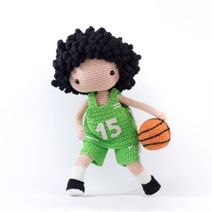 May include: A crocheted doll wearing a green basketball uniform with the number 15 on the front. The doll is holding an orange basketball.