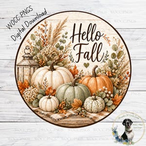 Op de afbeelding: Ronde houten bord met een herfstthema. Het bord toont de tekst "Hello Fall" met pompoenen, bladeren en bloemelementen. De pompoenen zijn wit, oranje en groen. Een lantaarn is ook inbegrepen.