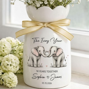 May include: A white ceramic vase with a scalloped rim and a light gold ribbon tied around the neck. The vase features a graphic of two elephants forming a heart with their trunks, the text The Ivory Year, 14 YEARS TOGETHER, Sophia, James, and 05.10.2026.