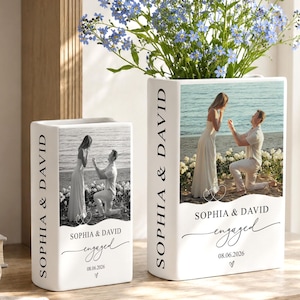 May include: Two white rectangular ceramic vases featuring a black and white engagement photo of a couple, the text "SOPHIA & DAVID" vertically on the side, and the text "SOPHIA & DAVID engaged 08.06.2026" on the front, filled with blue flowers.