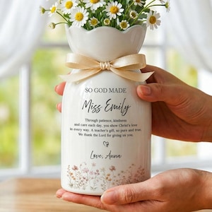 May include: A white ceramic vase filled with daisies, tied with a beige ribbon. The vase has the text "SO GOD MADE Miss Emily" and a personalized message. Floral design at the bottom. A thoughtful gift.