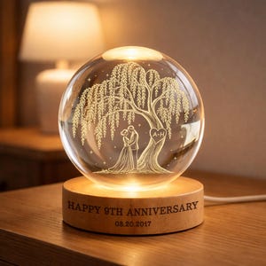 May include: A clear glass sphere lamp featuring an internal laser-etched willow tree and a couple standing beneath it. A heart with the letters A+H is etched on the tree trunk. The wooden base is engraved with HAPPY 9TH ANNIVERSARY 08.20.2017.