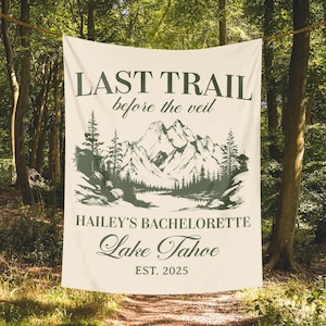 May include: Cream-colored banner with the text "LAST TRAIL before the veil" and "HAILEY'S BACHELORETTE Lake Tahoe EST. 2025". A mountain and forest graphic is printed below the text. The banner is hanging in a forest.
