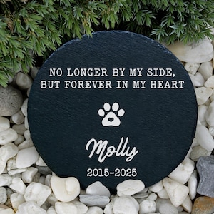 May include: A round, dark gray slate pet memorial stone with the text "NO LONGER BY MY SIDE, BUT FOREVER IN MY HEART." A paw print with a heart is centered above the name "Molly" and the years "2015-2025."