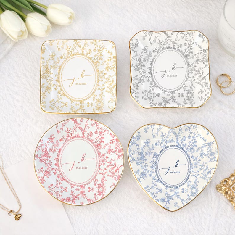 May include: Four decorative ceramic dishes in different shapes: square, scalloped, round, and heart-shaped. Each dish features a floral pattern in gold, gray, pink, and blue, with gold trim. The center of each dish has the initials "j.k" and the date "09.20.2025".