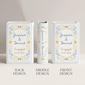 May include: A white rectangular ceramic vase featuring a floral wreath illustration in blue and yellow. The text reads Jessica & Daniel, Engaged, and 08.20.2026. The design is repeated on the front, back, and narrow side of the upright vase.