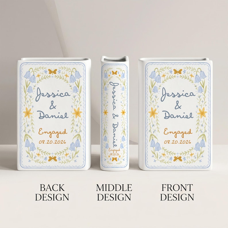 May include: A white rectangular ceramic vase featuring a floral wreath illustration in blue and yellow. The text reads Jessica & Daniel, Engaged, and 08.20.2026. The design is repeated on the front, back, and narrow side of the upright vase.