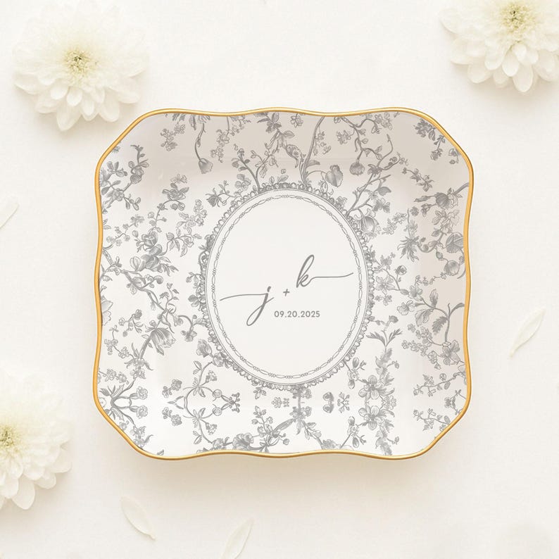 May include: A rectangular, white ceramic tray with a gold rim and a floral pattern in gray. The center features a circular design with the initials "j + k" and the date "09.20.2025".