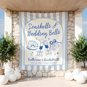 May include: A banner with blue and white stripes and the text "Seashells & Wedding Bells" in a script font. Below the text are illustrations of a seashell, champagne flutes, and bells. The banner reads "Katherine's Bachelorette, July 25, 2026, Miami, Florida."