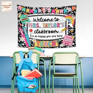 Puede incluir: Un tapiz de aula con el texto "Welcome to MRS. TAYLOR'S classroom" en un dise&ntilde;o colorido. El tapiz presenta un patr&oacute;n floral en blanco y negro, un arco&iacute;ris y la palabra "TEACH". Una mochila azul est&aacute; sobre una silla verde.