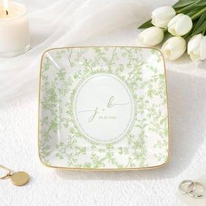 May include: Square ceramic trinket dish with a green floral pattern and gold trim. The center features the initials "J + K" and the date "09.20.2025" in a circular design. The dish is on a white surface.