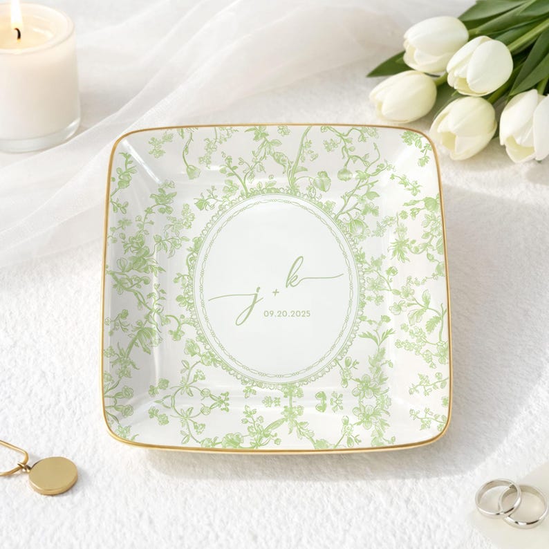 May include: Square ceramic trinket dish with a green floral pattern and gold trim. The center features the initials "J + K" and the date "09.20.2025" in a circular design. The dish is on a white surface.