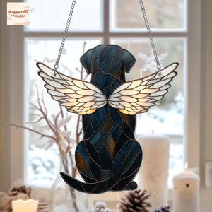 May include: Stained glass window decoration featuring a black dog with white angel wings. The dog is in a sitting position, with the wings positioned behind its back. The glass has a mosaic pattern with shades of blue and brown. The decoration hangs from a silver chain.