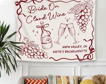 May include: Off-white wall tapestry with a burgundy border and illustrations of wine-related elements. The text "Bride On Cloud Wine" is displayed, along with a wine bottle, champagne glasses, and grapes. The text "Napa Valley, CA Katie's Bachelorette" is also included.