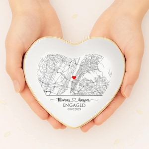 May include: A heart-shaped white ceramic dish with a gold rim, featuring a black and white map design and a red heart. The text reads "thomas & harper ENGAGED 03.02.2025".