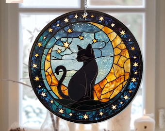 May include: A stained glass suncatcher featuring a black cat sitting on a crescent moon with a blue and yellow background. The suncatcher is surrounded by a border of stars.