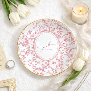 May include: A white ceramic plate with a pink floral design and gold trim. The plate features the initials "j + k" and the date "09.20.2025" in the center. The plate is surrounded by white tulips and a lit candle.