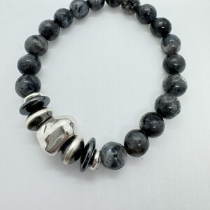 Op de afbeelding: Een zwarte kralen armband met een zilveren hartvormige hanger en zwarte kralen. De armband is gemaakt van natuurlijke stenen en is een stijlvol accessoire.