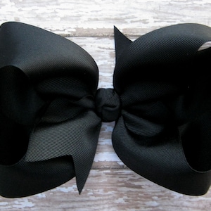 May include: A large black hair bow made from grosgrain ribbon. The bow is tied in a classic style with two loops and a center knot.