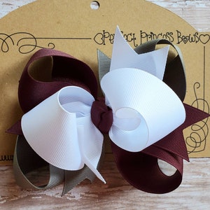 May include: A burgundy, white, and gray hair bow with a center knot. The bow is on a brown card with the text "Perfect Princess Bows" in black.