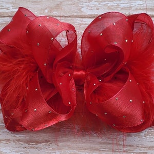 May include: A red satin and tulle bow with silver glitter accents and red feathers.