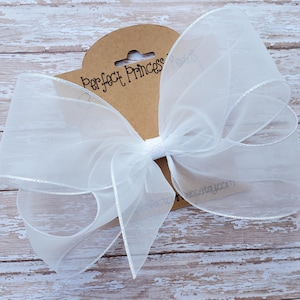 May include: A large white tulle bow with silver edging. The bow is tied with a white ribbon and has a brown tag that says "Perfect Princess" on it.